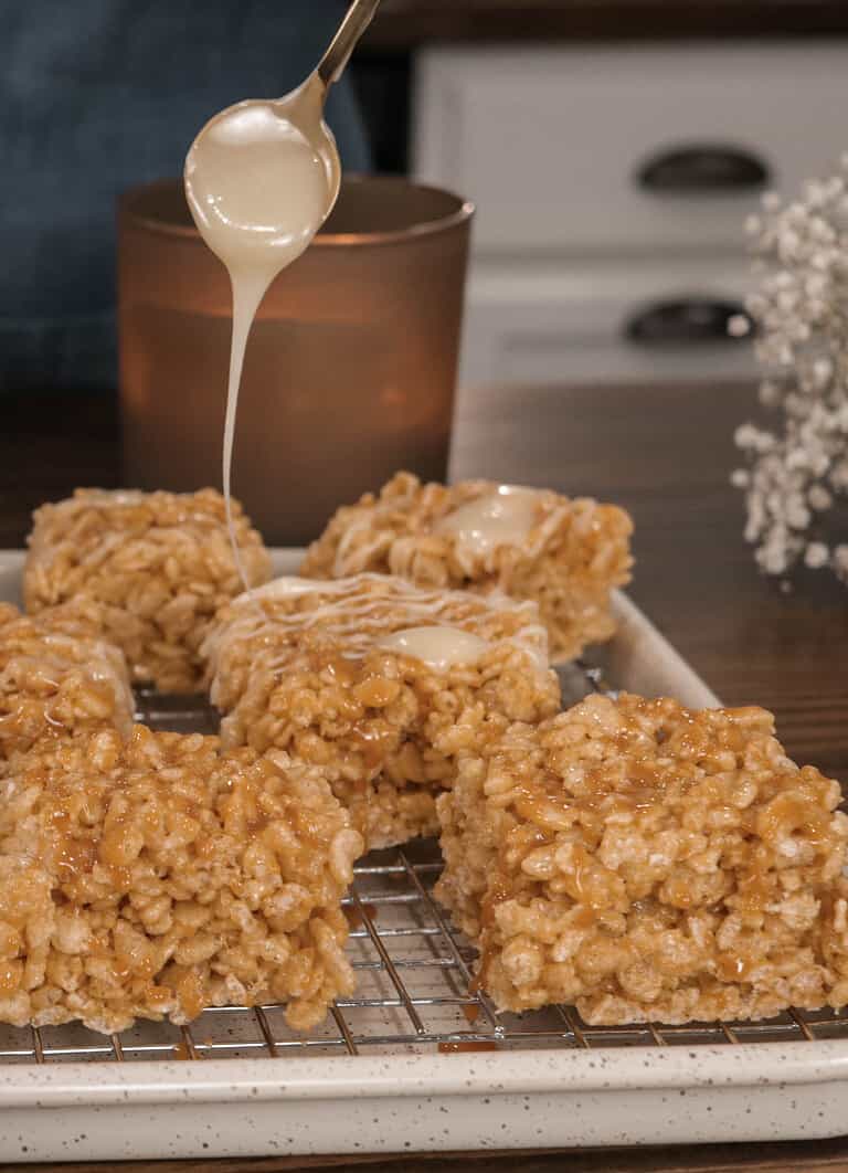 Pumpkin Spice Rice Krispie Squares on a wire rack with a gold spoon drizzling melted white chocolate on top of them.