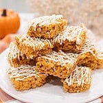 Stack of pumpkin spice Rice Krispie treats drizzled with white chocolate on a white plate with a soft autumn background