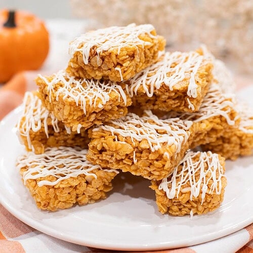 Stack of pumpkin spice Rice Krispie treats drizzled with white chocolate on a white plate with a soft autumn background