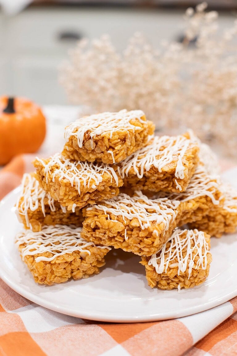 Stack of pumpkin spice Rice Krispie treats drizzled with white chocolate on a white plate with a soft autumn background