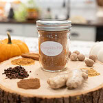 Homemade pumpkin pie spice displayed in a mason jar with lid, styled with cinnamon sticks, cloves, ginger, nutmeg, and fall decor in a cozy kitchen setting