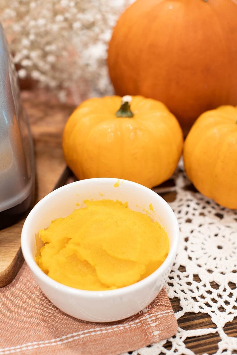 Homemade pumpkin puree in a white bowl with whole pie pumpkins on a rustic table