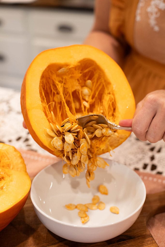 Scooping pumpkin seeds and pulp from a halved pumpkin before baking