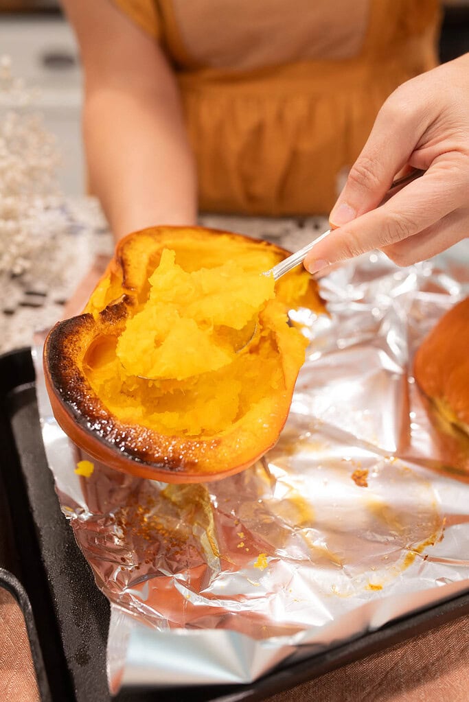 Roasted pumpkin being scooped from the skin on a foil-lined baking sheet