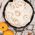 Sourdough pumpkin cinnamon rolls with cream cheese frosting in cast iron skillet on lace table