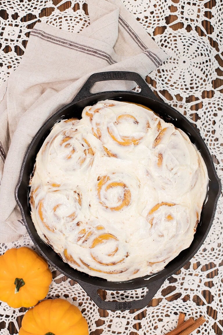 Sourdough pumpkin cinnamon rolls with cream cheese frosting in cast iron skillet on lace table