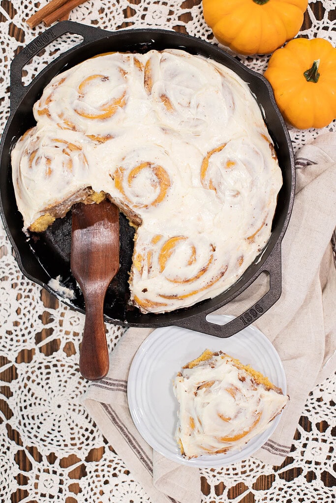 Sourdough pumpkin cinnamon rolls with cream cheese frosting and slice removed in cast iron skillet