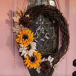 A beautiful front door fall wreath on a pink door on a sage green cottage.