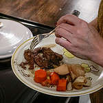 A woman is making a plate of roast beef from a dutch oven on top of a stove.