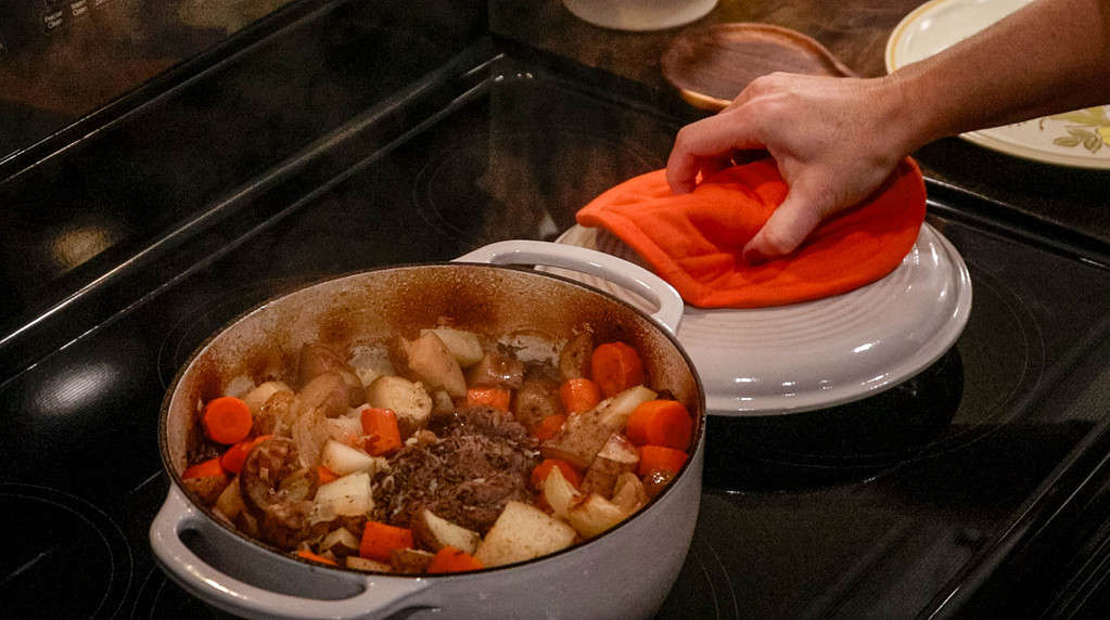 A off white dutch oven on a stove top with beef roast and veggies cooked in it.