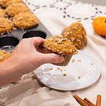 Hand holding sourdough pumpkin muffin with oat streusel topping over plate and kitchen cloth