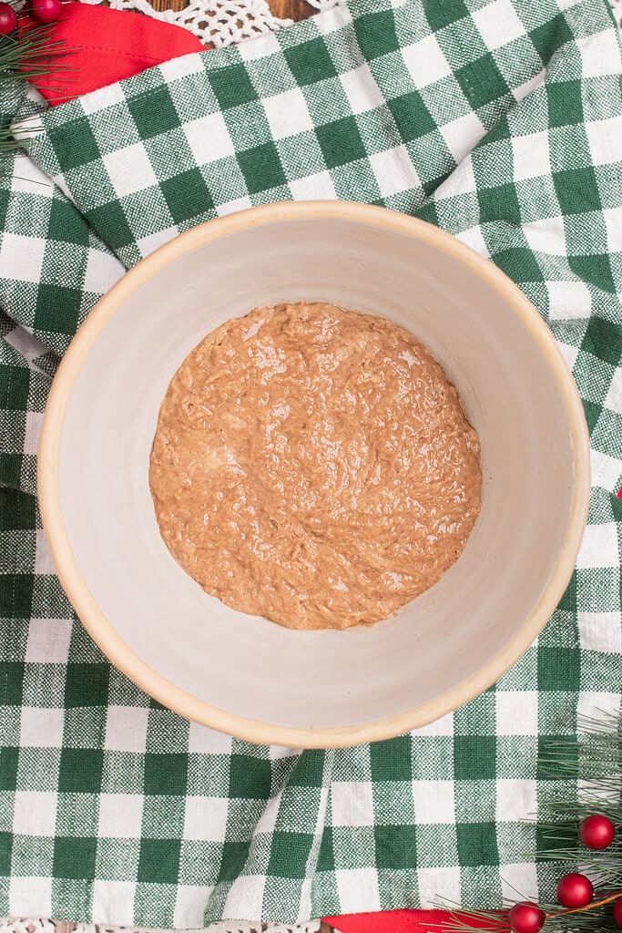 Overhead view of active sourdough starter in a cream mixing bowl, ready to use in sourdough fruitcake batter, on a green gingham cloth with holiday greenery