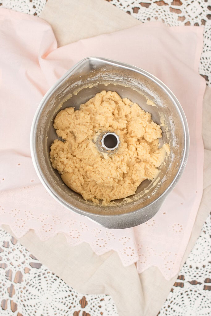 Overhead view of finished spritz cookie dough in a stand mixer bowl, ready to load into a cookie press, on a pink eyelet linen