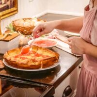 a women in a cottage kitchen drizzling strawberry compote on a einkorn dutch baby pancake