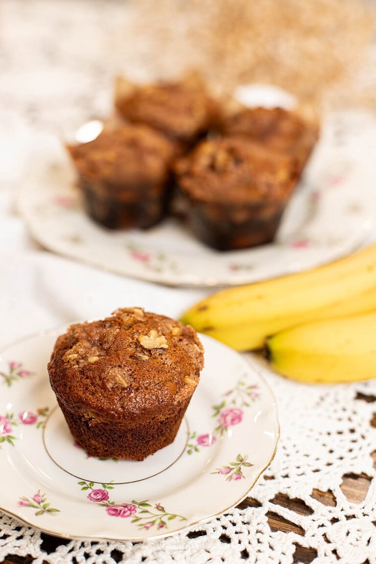 Sourdough banana muffin on a floral plate with ripe bananas and additional muffins in the background.