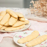 Two floral china plates of sourdough ladyfingers on a pink linen -- a large plate piled high and a small plate with two ladyfingers -- with dried baby's breath in the background