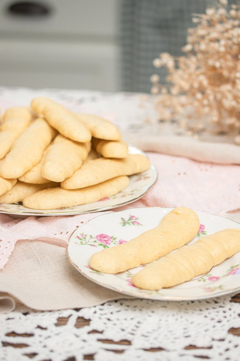 Two floral china plates of sourdough ladyfingers on a pink linen -- a large plate piled high and a small plate with two ladyfingers -- with dried baby's breath in the background