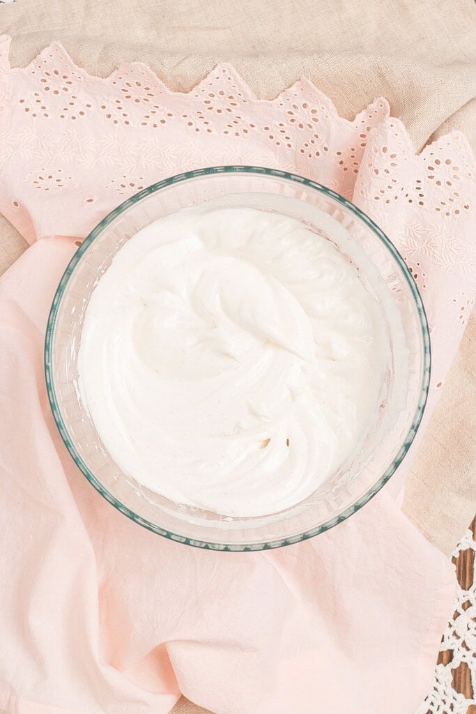 Overhead view of whipped cream at stiff peaks in a glass bowl, on a pink eyelet linen and lace doily