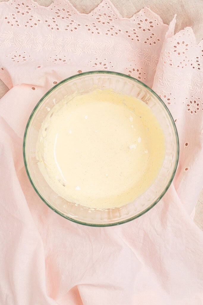 Overhead view of whipped mascarpone and cream mixture in a glass bowl, on a pink eyelet linen and lace doily