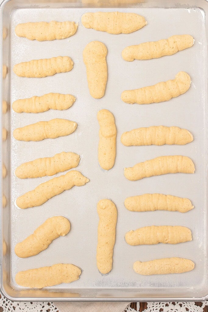 Overhead view of a full silver baking sheet of baked sourdough ladyfinger cookies on parchment paper