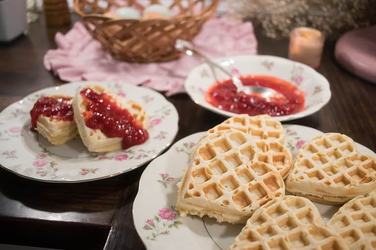 sourdough waffles on a china plate beside another plate of waffles topped with strawberry compote