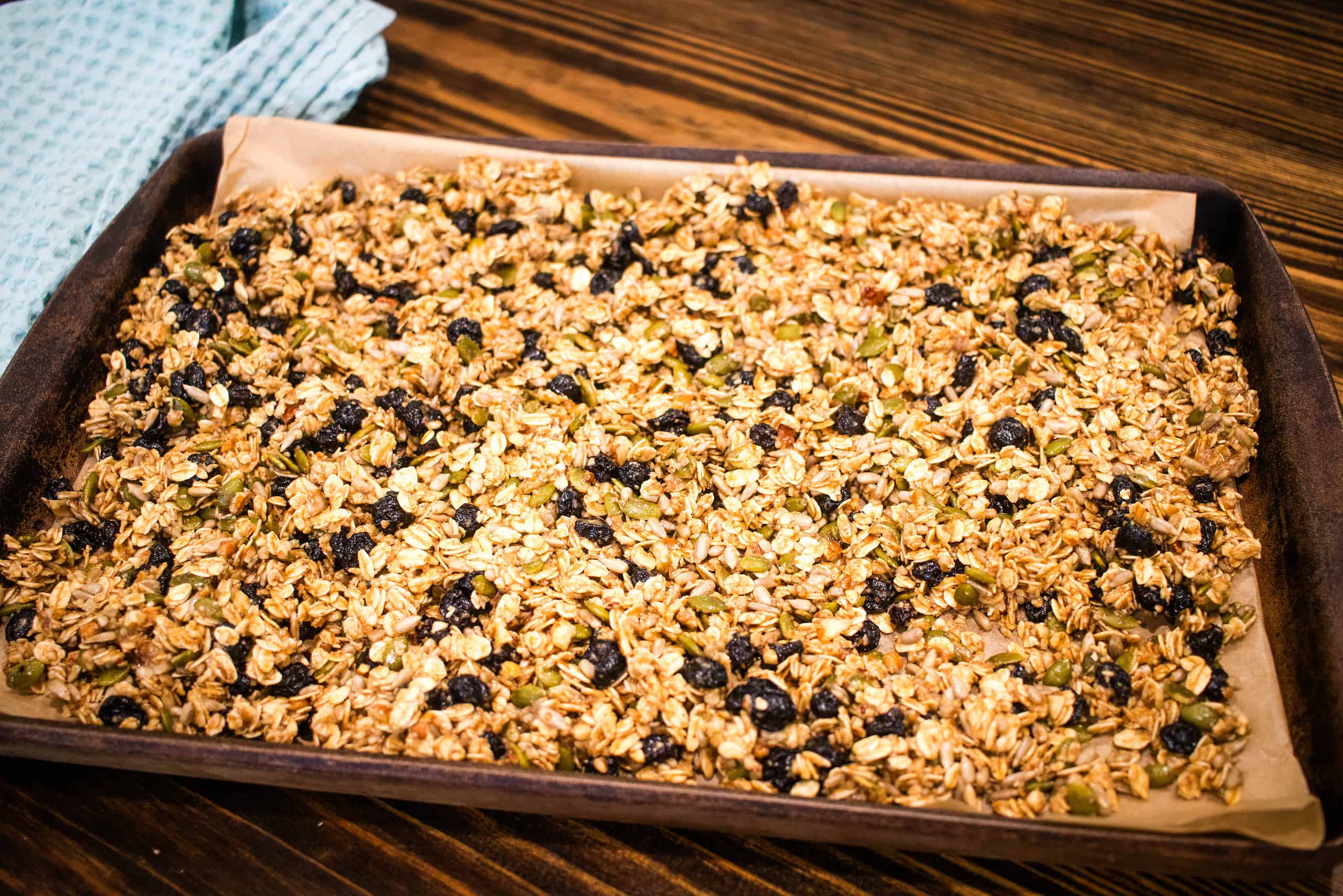 A ceramic pan of homemade sourdough granola on a wooden counter top in a cottage kitchen.