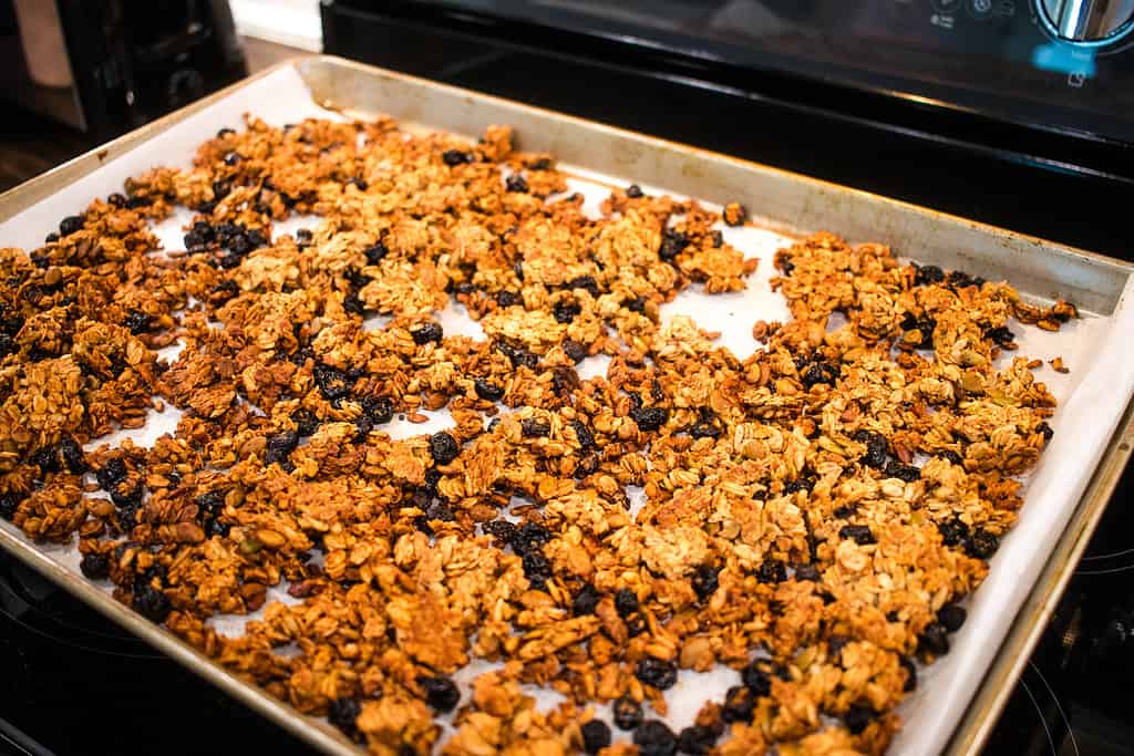 A pan of coked granola homemade in a cottage kitchen on a silver baking pan.