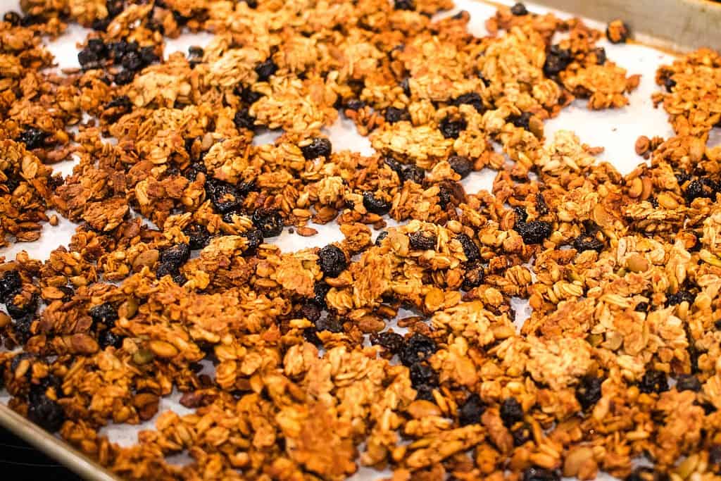 A pan of coked granola homemade in a cottage kitchen on a silver baking pan.