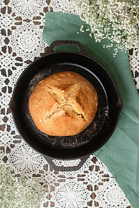 Freshly baked sourdough Irish soda bread in a cast iron skillet with a deep cross cut across the golden crust.