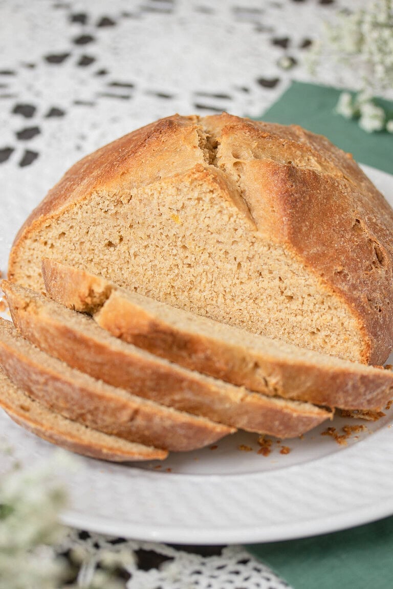 Sliced loaf of sourdough Irish soda bread on a white plate showing the tender crumb and rustic crust.