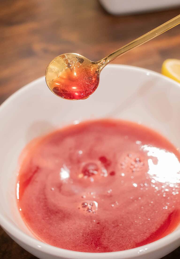 a women drizzling strawberry simple syrup over a white bowl filled with strawberry simple syrup