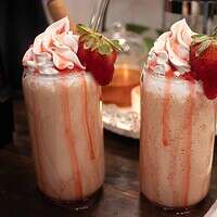 two strawberry frappucinos topped with whipped cream drizzled with strawberry simple syrup