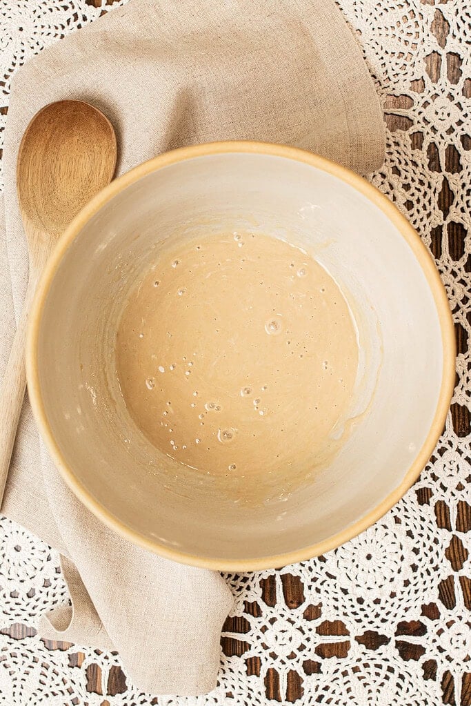 Wet mixture of sourdough starter, maple syrup, coconut oil, and vanilla in a mixing bowl for sourdough granola.