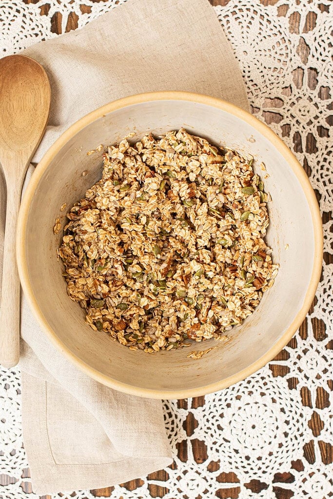 Unbaked sourdough granola mixture of oats, nuts, and seeds coated evenly in maple and starter mixture in a large bowl.