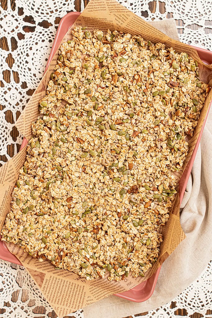 Freshly baked sourdough granola cooling in a baking pan before being broken into clusters.