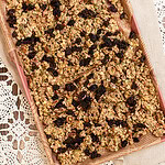 Sourdough granola spread on a parchment-lined baking sheet, filled with rolled oats, pecans, pumpkin seeds, sunflower seeds, and raisins baked into golden clusters.