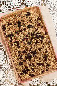 Sourdough granola spread on a parchment-lined baking sheet, filled with rolled oats, pecans, pumpkin seeds, sunflower seeds, and raisins baked into golden clusters.