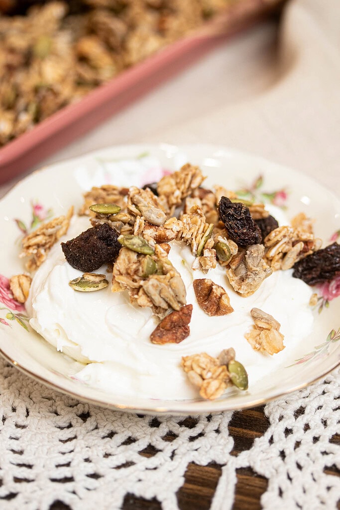 Close-up of sourdough granola clusters with oats, seeds, pecans, and raisins on top of yogurt.