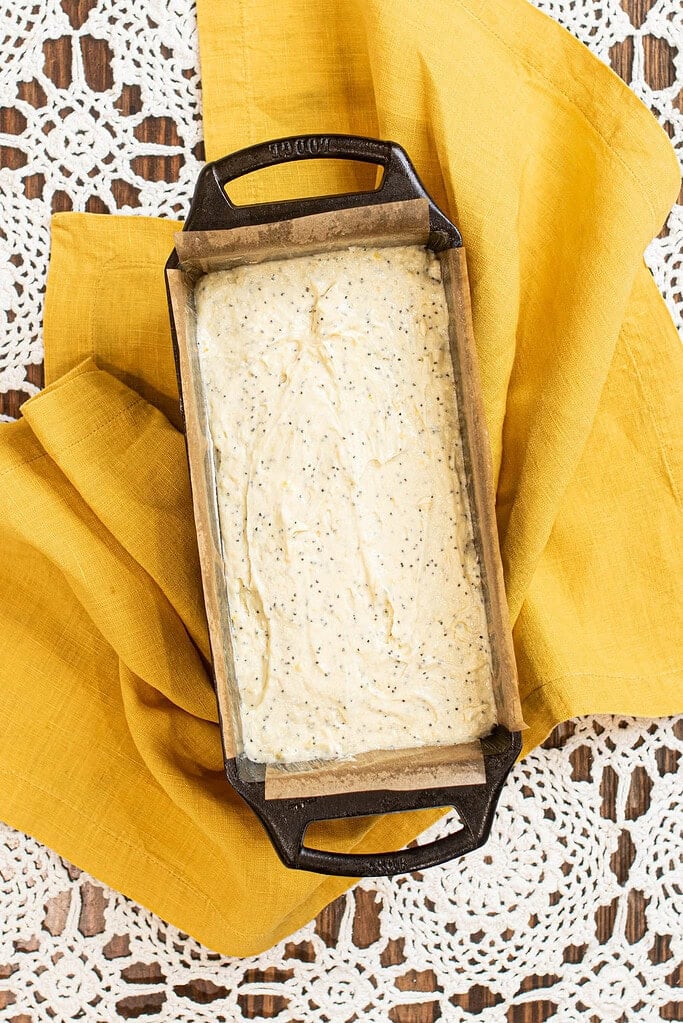 Sourdough lemon poppy seed pound cake batter spread evenly in a parchment-lined loaf pan before baking.