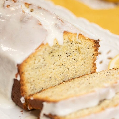 Close-up of sliced sourdough lemon poppy seed pound cake showing moist crumb and lemon glaze dripping over the edges.