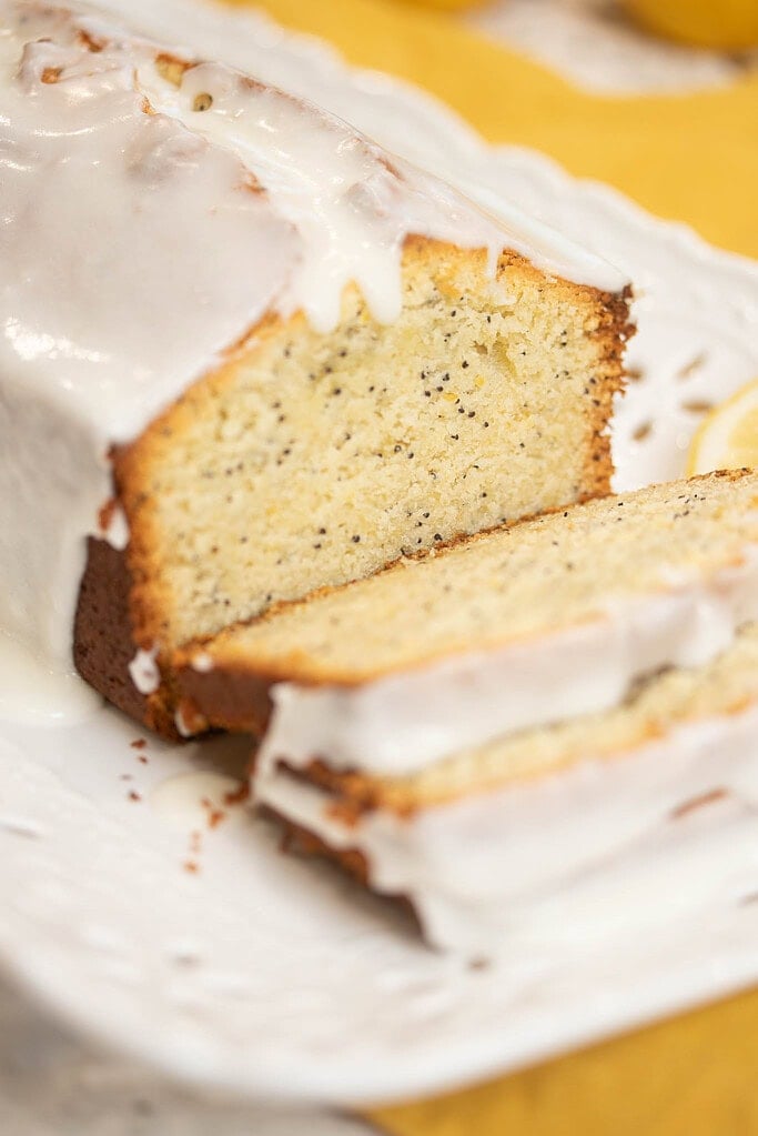 Close-up of sliced sourdough lemon poppy seed pound cake showing moist crumb and lemon glaze dripping over the edges.