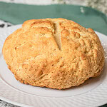 Freshly baked traditional Irish soda bread with a golden crust and a deep cross cut on top, sitting on a white plate with a green linen napkin on a lace tablecloth.