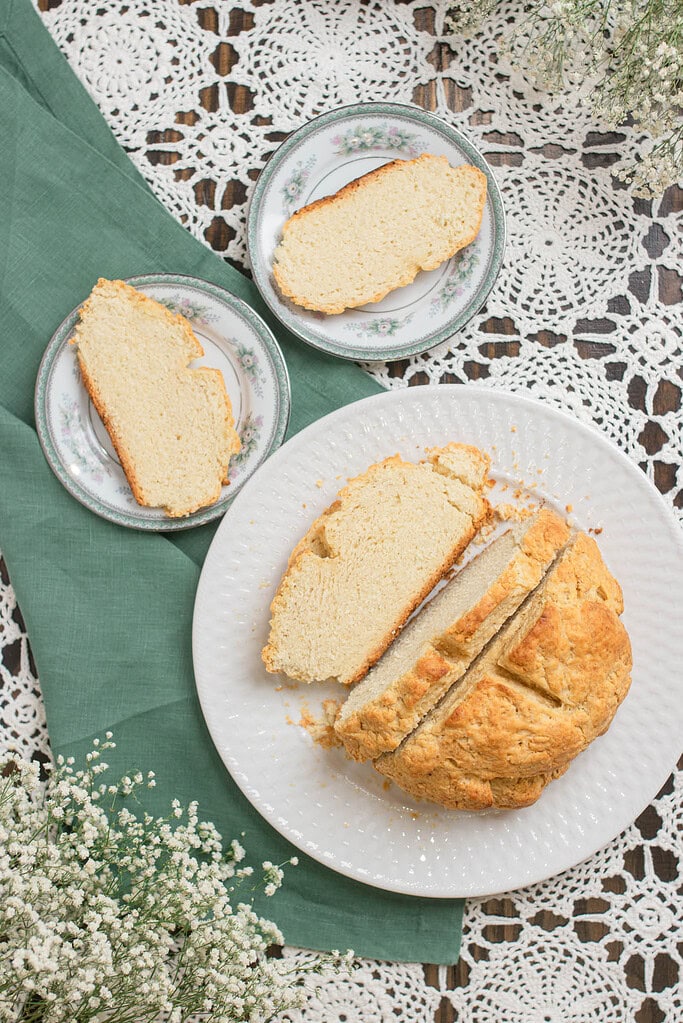 Sliced Irish soda bread arranged on plates, showing the soft crumb inside the loaf and several slices beside it on a lace-covered table.