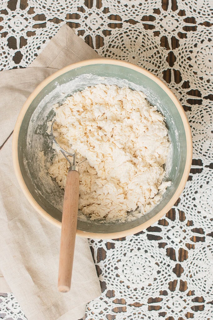 Thick Irish soda bread dough partially mixed in a bowl with a dough whisk, showing the rough texture before shaping.