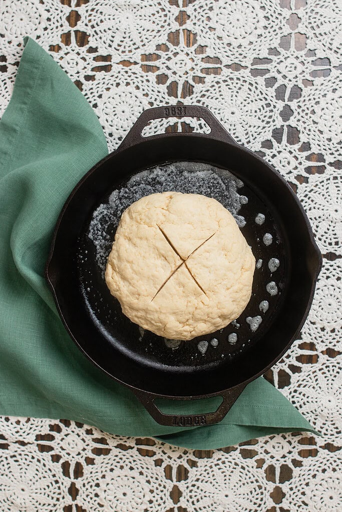 Round Irish soda bread dough placed in a cast iron skillet and scored with a cross on top before baking.