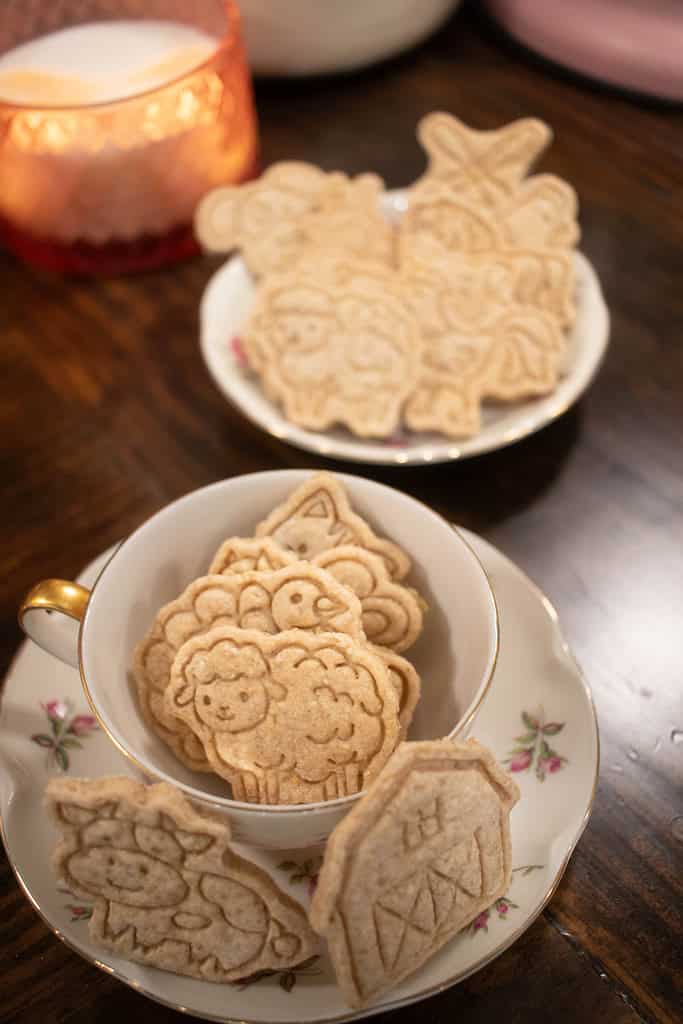 a vertical image of animal crackers in a pink floral china cup on a wooden countertop in a cottage kitchen