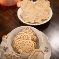 a vertical image of animal crackers in a pink floral china cup on a wooden countertop in a cottage kitchen