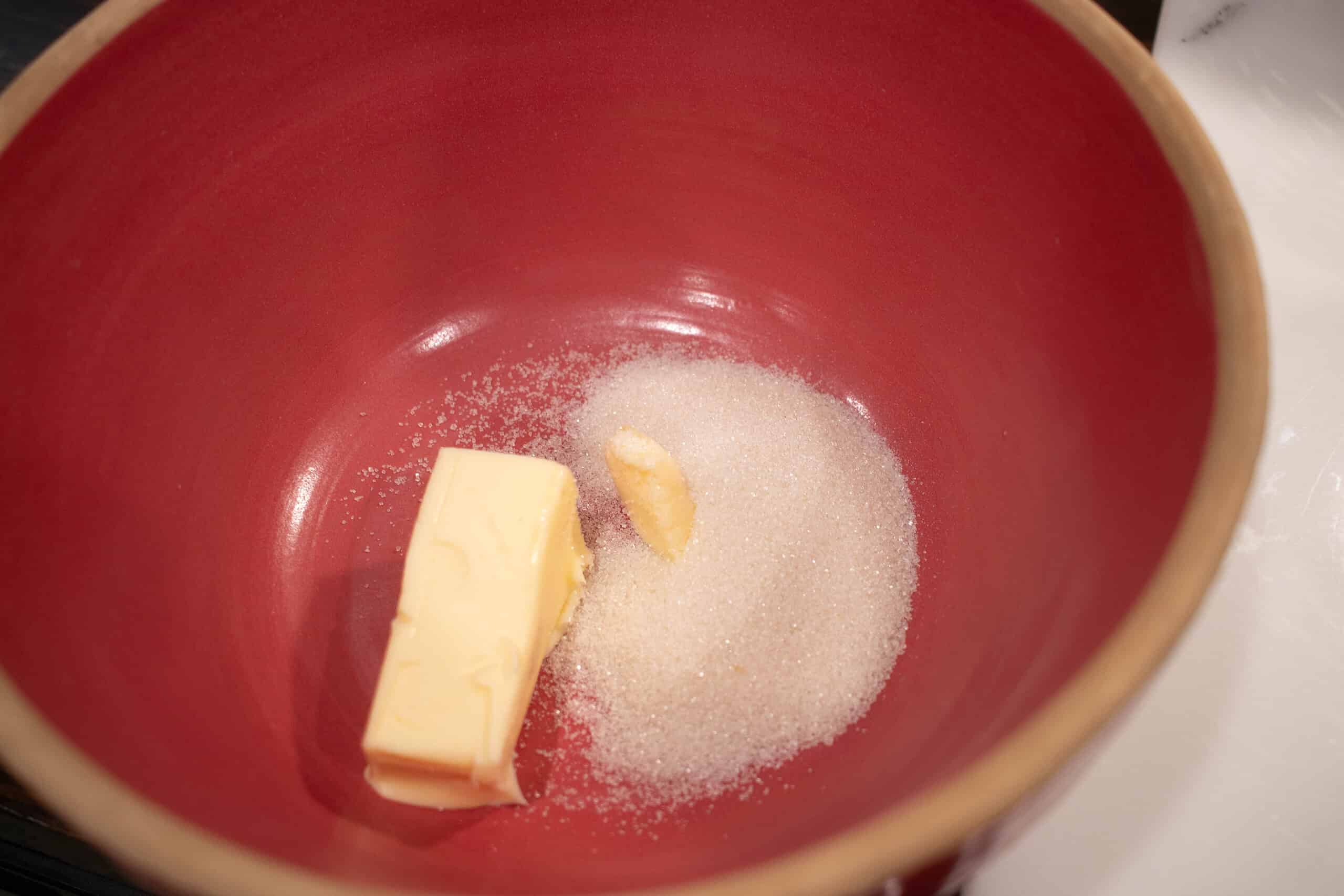 A pink ceramic bowl with butter and granulated sugar in a cottage kitchen on a counter top.