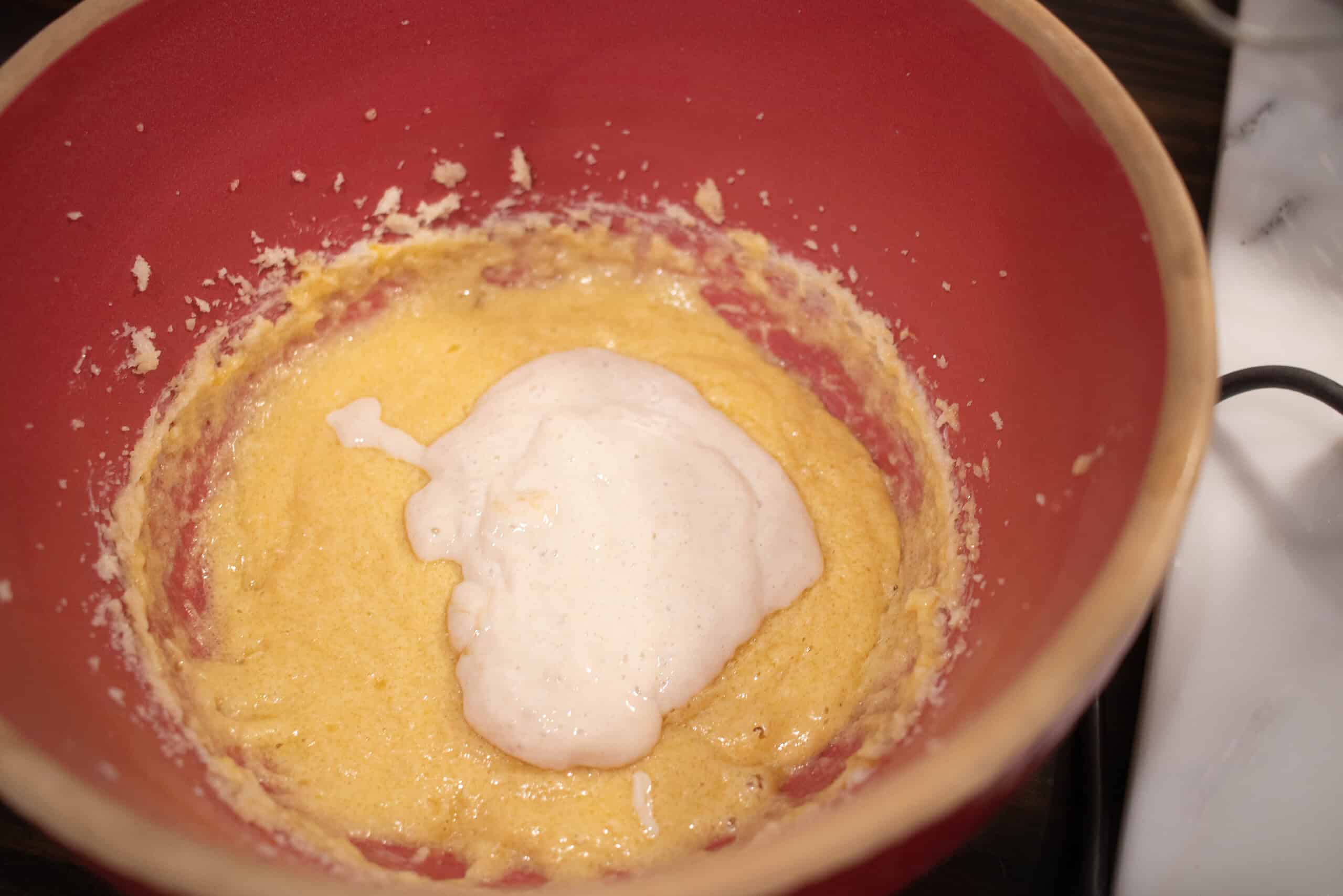 a pink ceramic bowl with mixture of wet ingrediats for sourdough animal crackers with a dollop of sourdough starter in the bowl