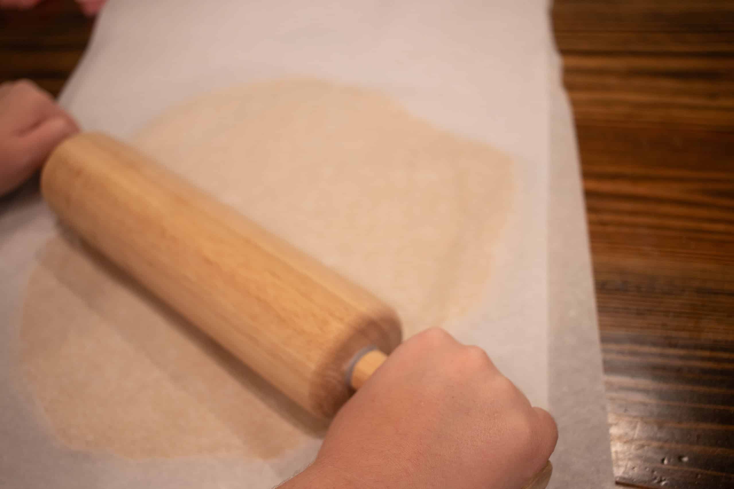 a women rolling out dough for animal crackers on a wooden countertop